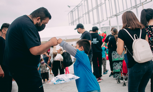 A man in a black kn95-style mask fist bumps a small child